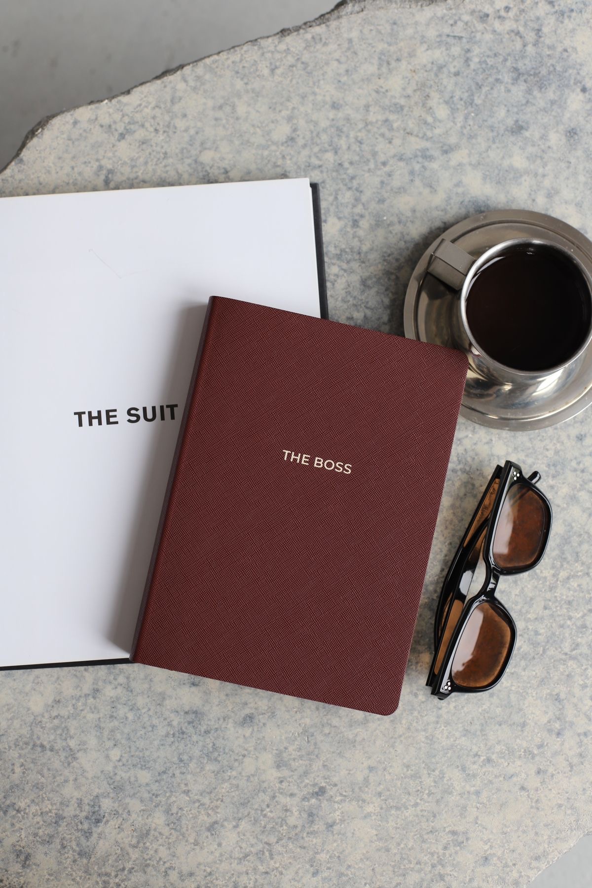 Caderno The Boss ao lado de café e óculos